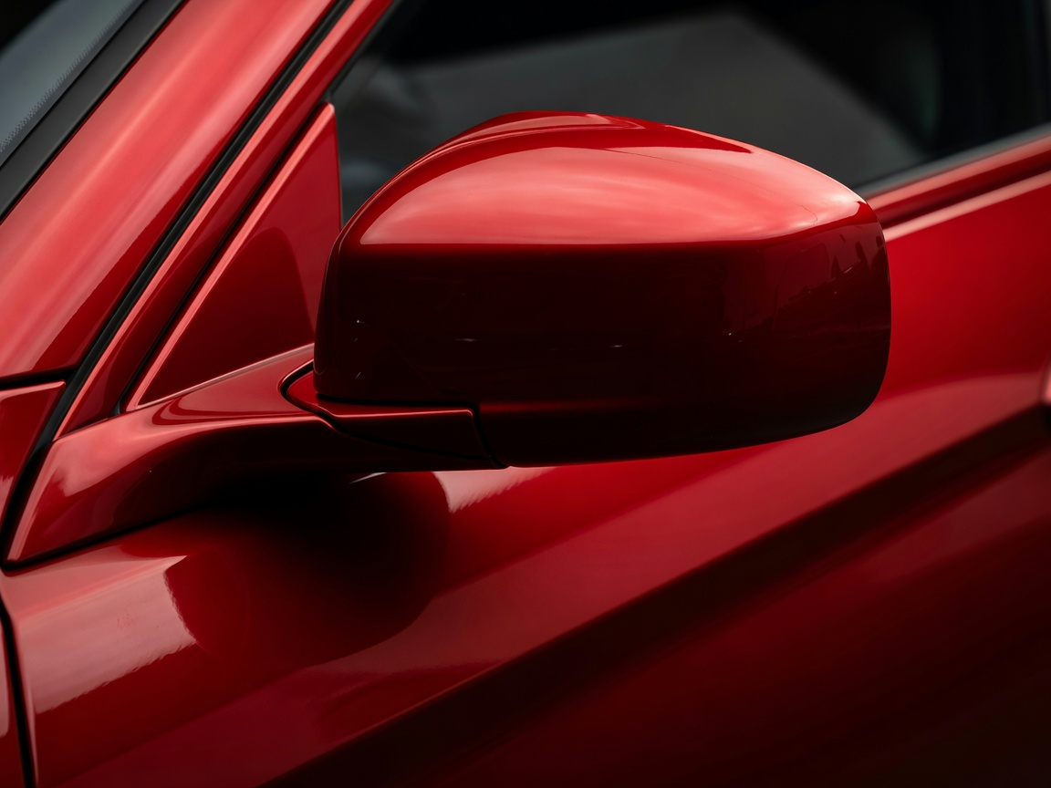 High-contrast mirror reflection on a red car wing after a dual-stage paint correction process highlighting zero swirl marks